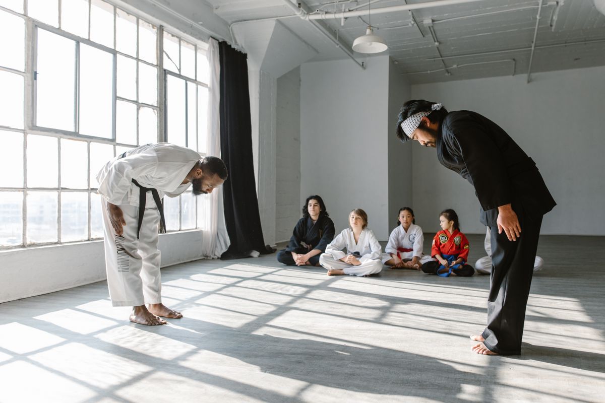 Two instructors bowing to each other while young students watch from the mat
