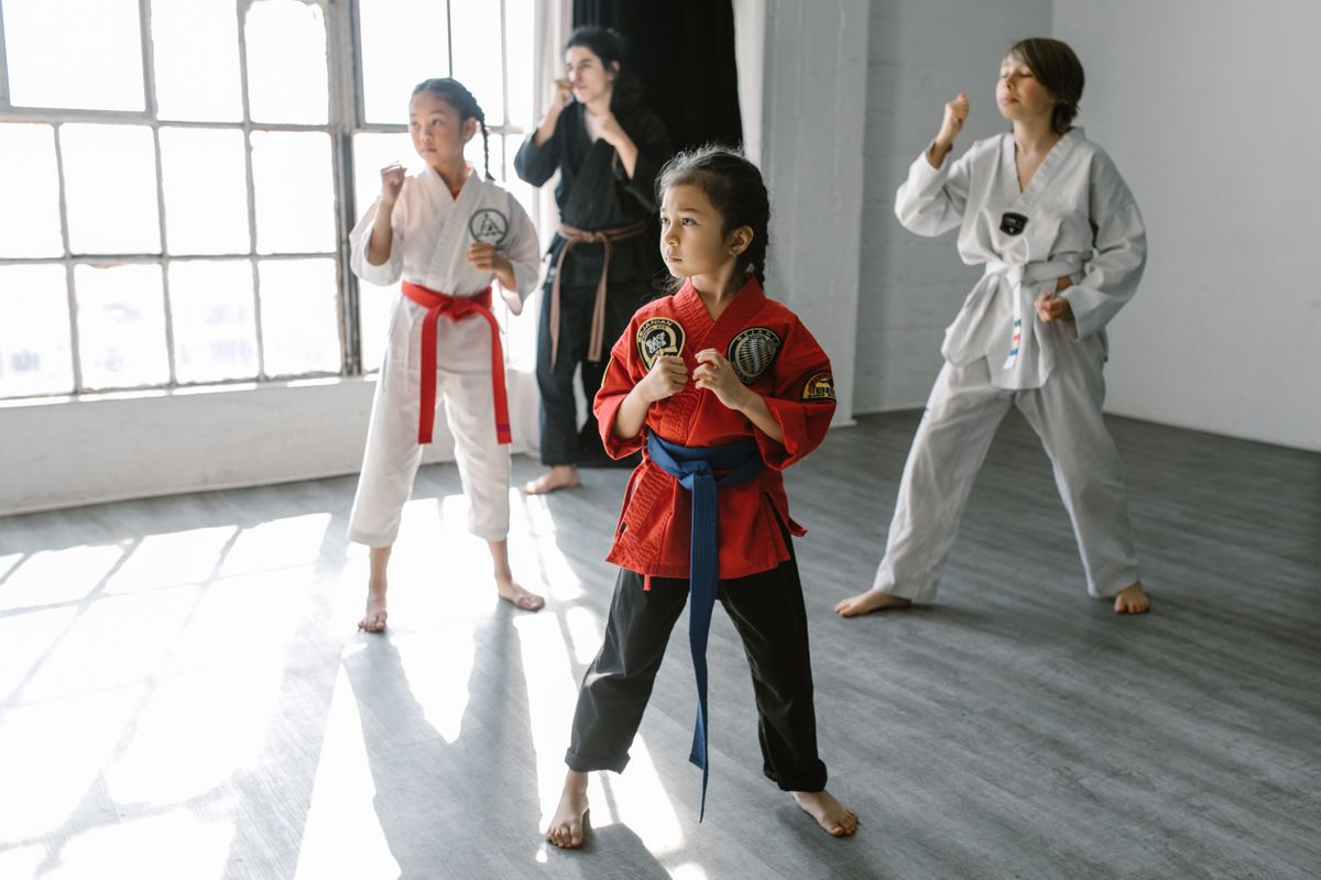 Kids martial arts class in a sunlit dojo, students in gis practicing stances together