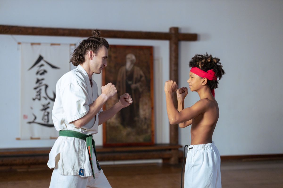Instructor coaching a young student in a sparring stance inside a traditional dojo