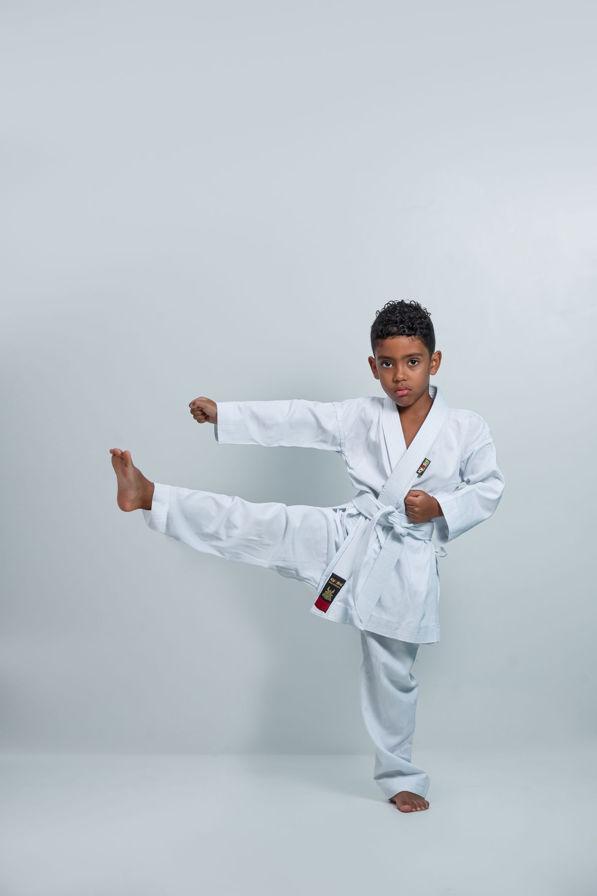 Child in a white gi executing a high side kick with concentration