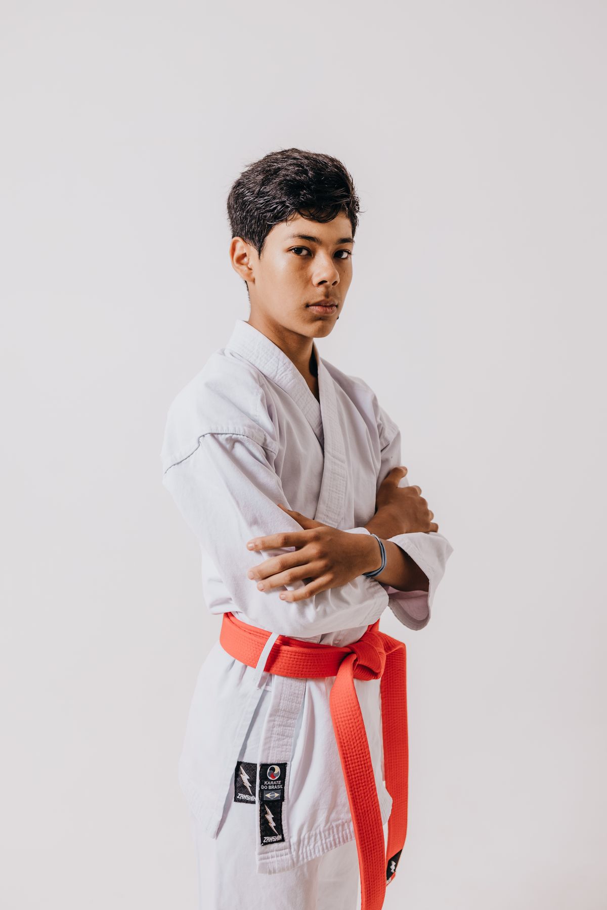 Teen martial arts student in a gi with an orange belt, arms crossed and confident